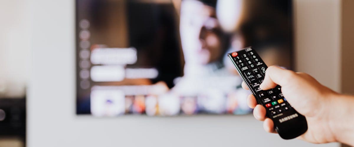 Hand holding a TV remote in front of a screen showing an IPTV channel guide
